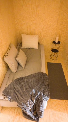 Low retreat bed with beige cushions and a small bedside table, viewed from above.