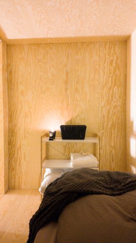 Low bed beside built-in wooden shelves in the warm cabin interior.