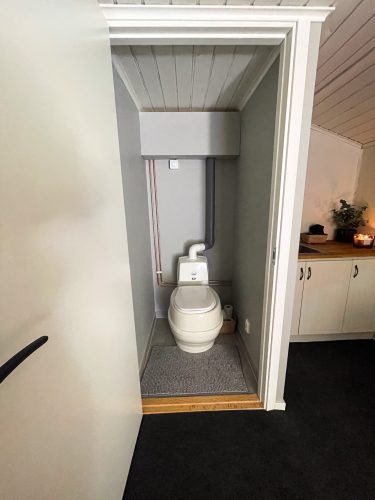 Compact private toilet room with a white composting toilet.