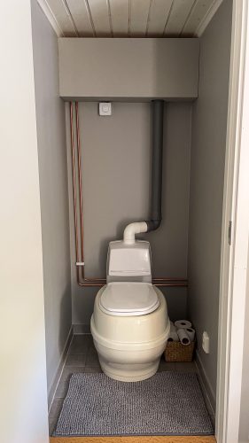 White composting toilet in a compact cabin washroom.