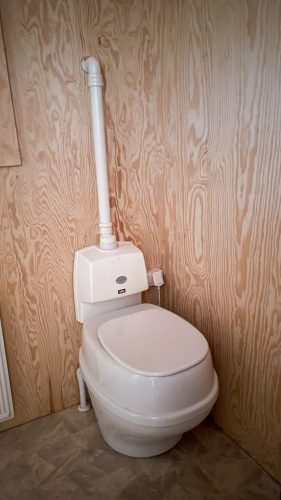 White composting toilet set against a wood-panelled wall.