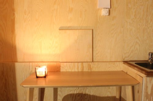 Lit candle resting on a long wooden shelf against the cabin’s wood-panelled wall.