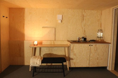 Simple wooden writing desk with a chair and candle against a wood-panelled wall.