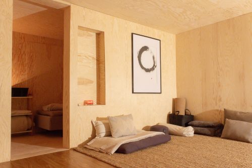 Low bed with cushions in a wood-lined room beside an open doorway.